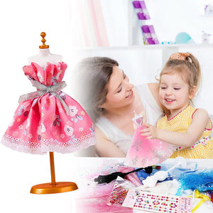 Child and mother using a fashion design studio kit with a pink floral fabric dress on a mannequin and assorted craft supplies on the table